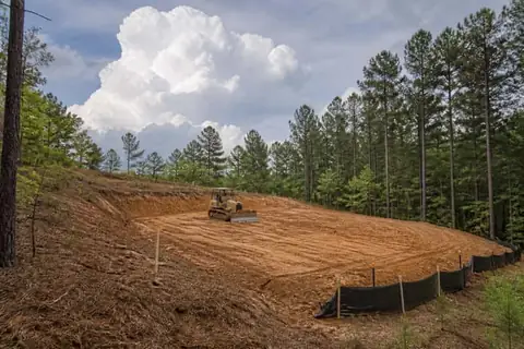 Small dozer shaping red sandy soil on a gently sloped East Texas homesite with silt fence on the low side